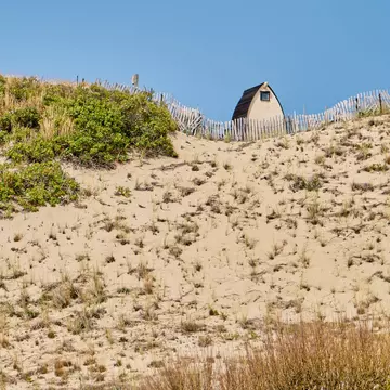 A structure at the top of a grassy and sandy dune under blue sky.
