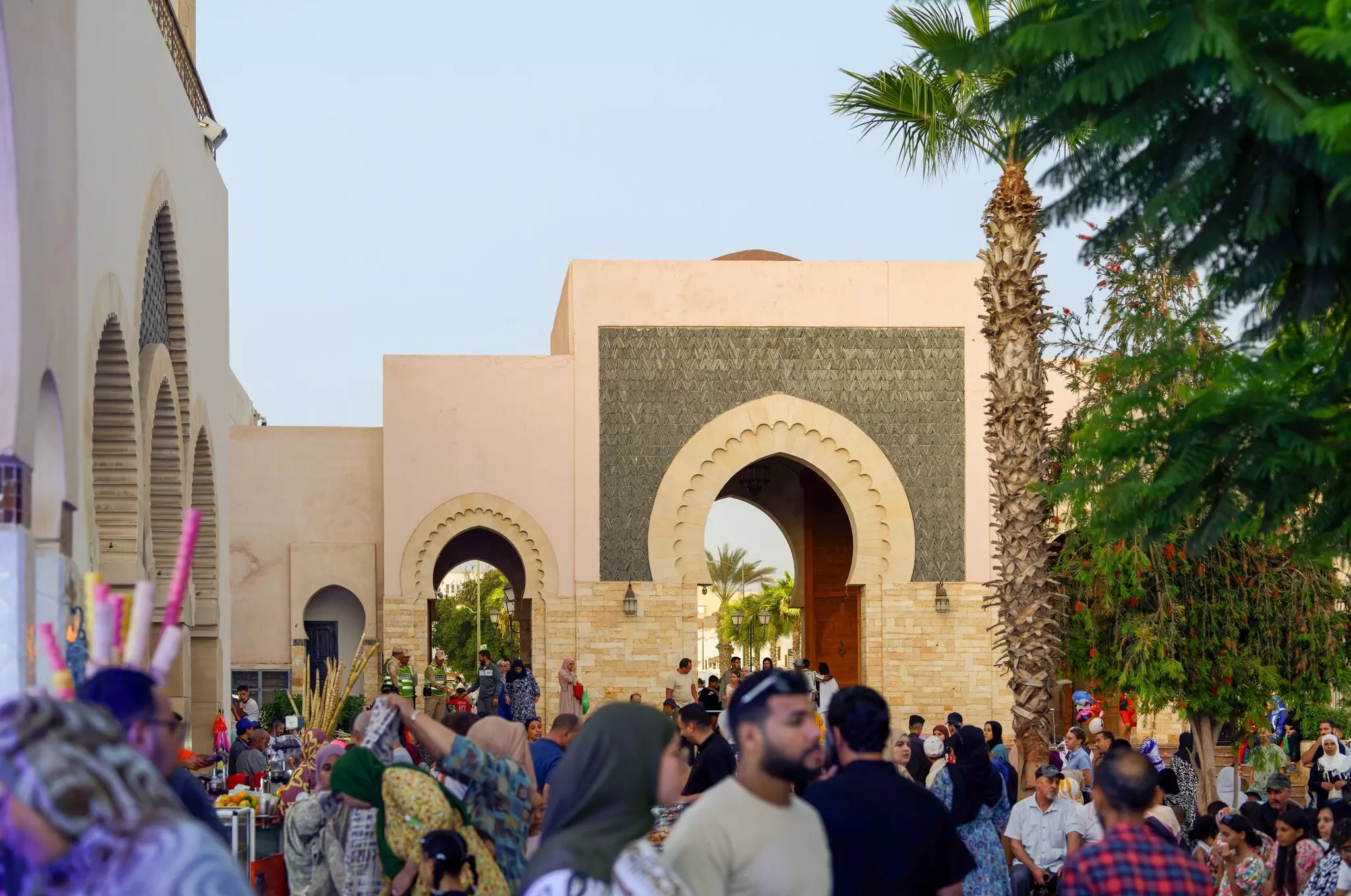 People in a bazaar in Morocco; an Islamic archway and palm trees are in the background.