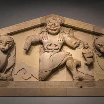 Carved limestone relief of a grimacing snake-belted figure flanked by two crouching big cats