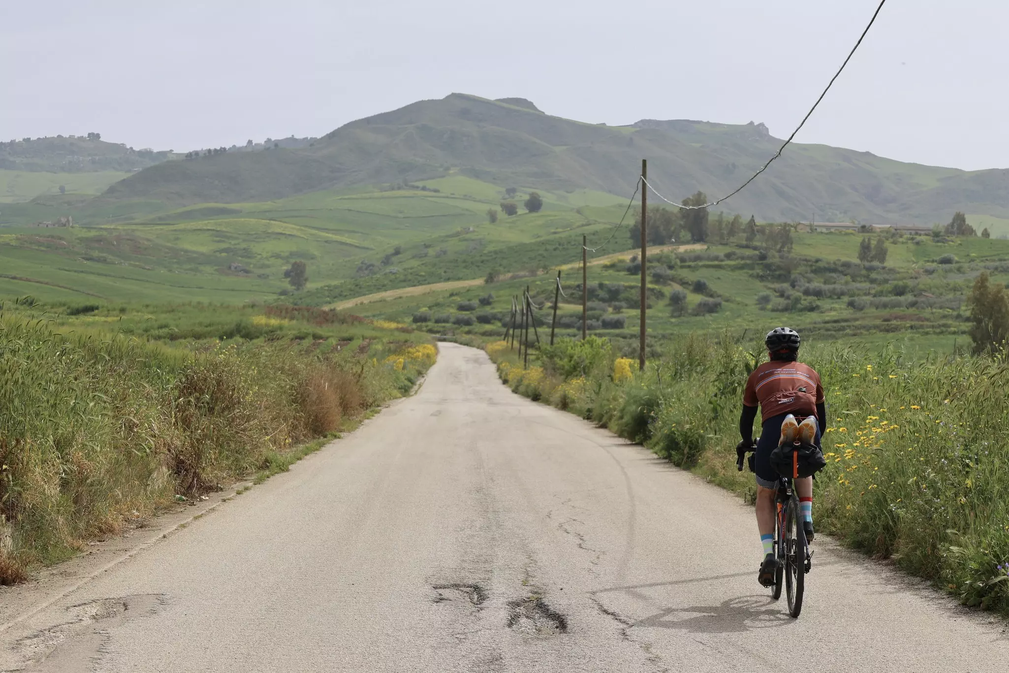 A cyclist on an asphalt road through green rolling hills.