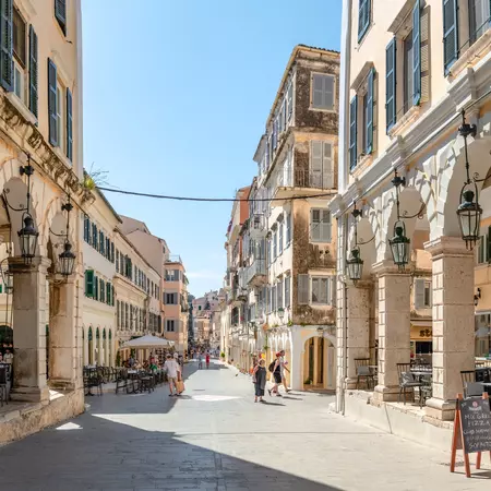 White buildings with high arches line a historic road in Greece.