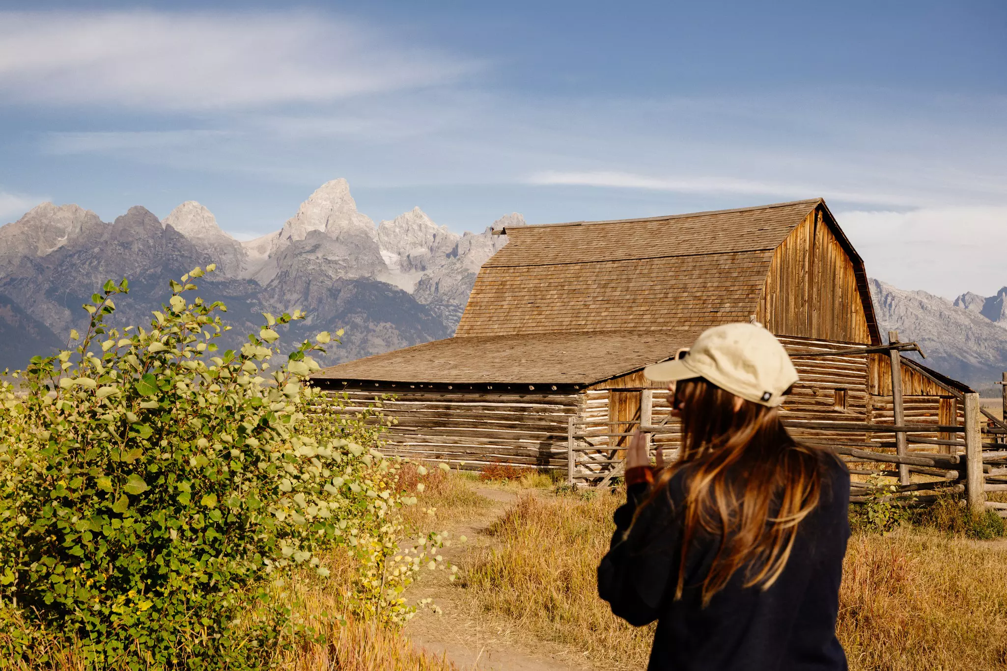 A woman in a baseball cap looking out toward a wooden barn and mountains