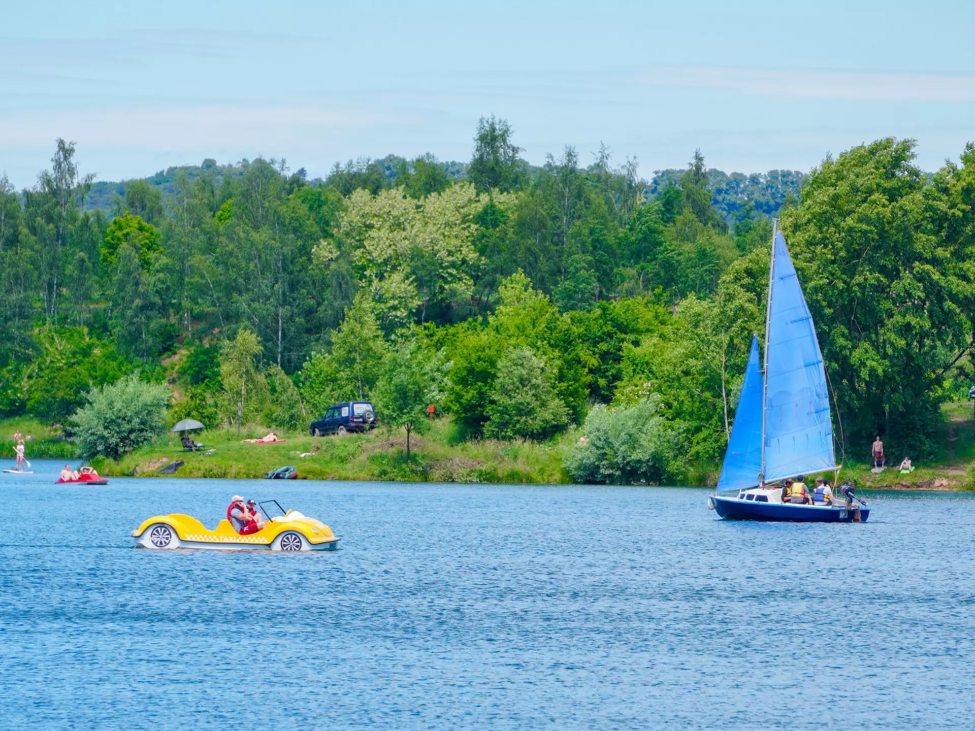 A small sail boat and a peddle boat on a lake on a summer's day