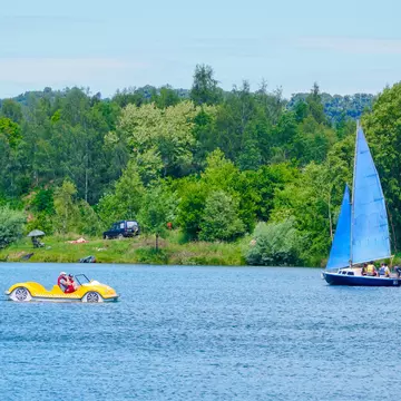 A small sail boat and a peddle boat on a lake on a summer's day