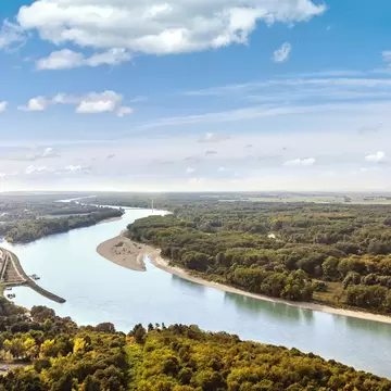 Danube river bending past a sandbank and dense riverside woodland in Nationalpark Donau-Auen, Hainburg town at left