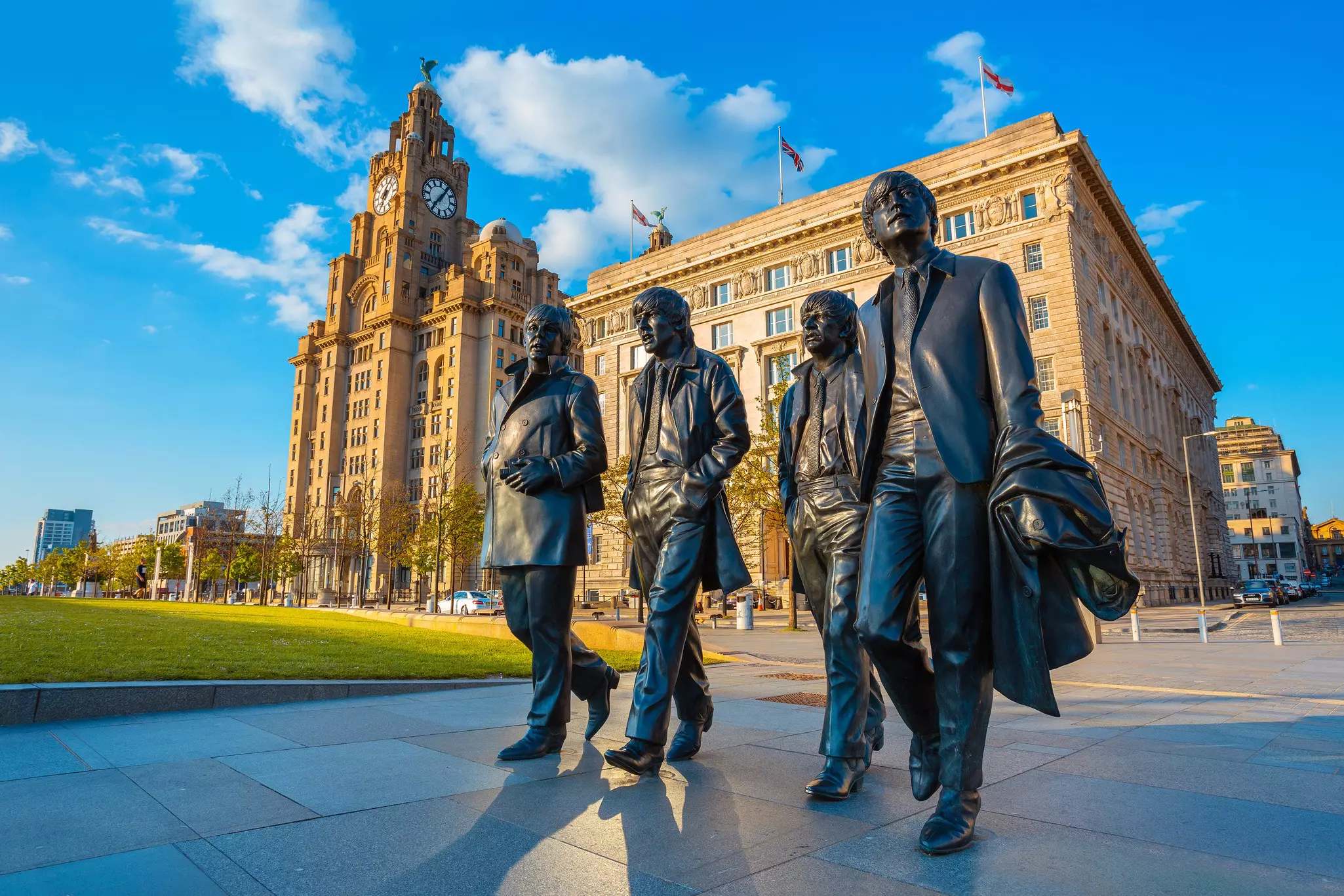 A bronze statue of four men walking in front of a city building with a clock tower.
