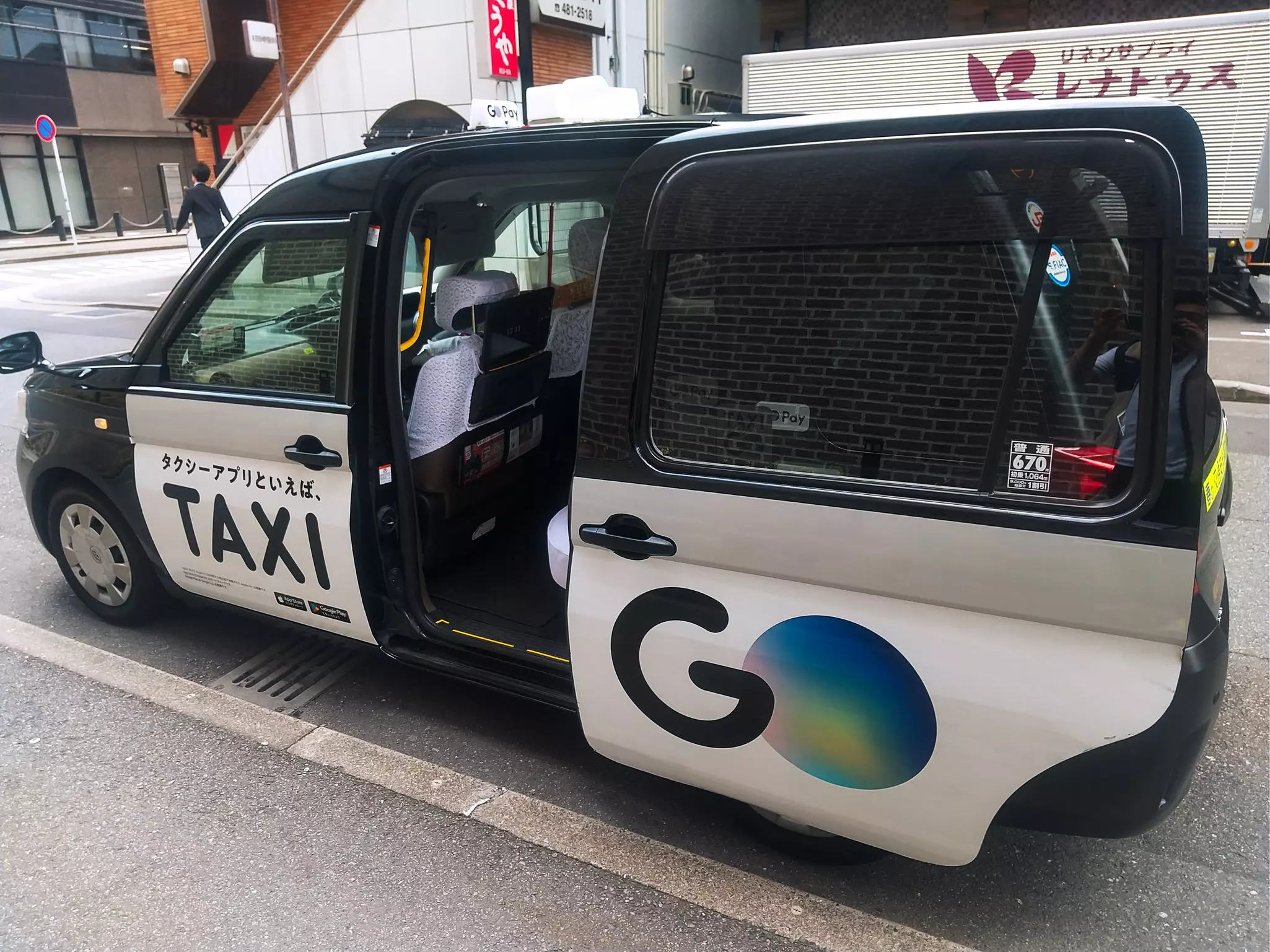 The left-hand door of a taxi that has opened automatically while the car is parked by the sidewalk