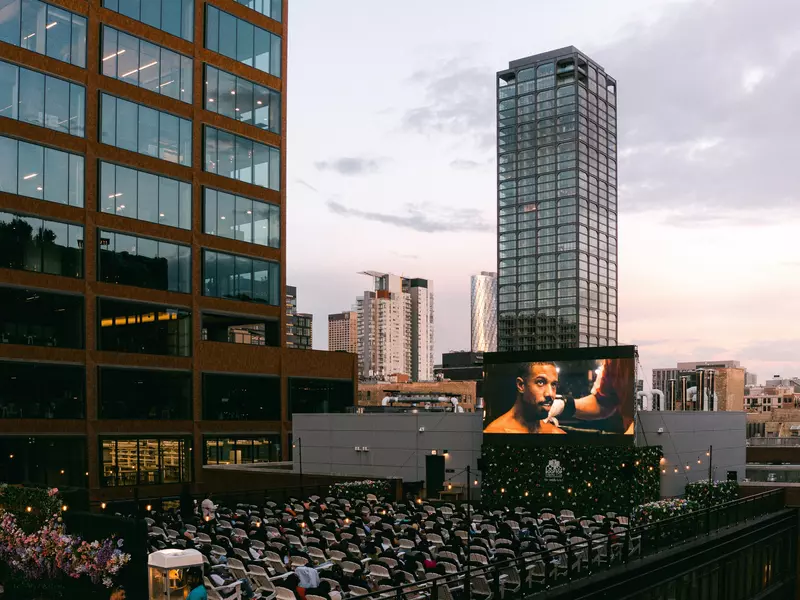 Seats set up on a rooftop facing a large screen showing a movie.