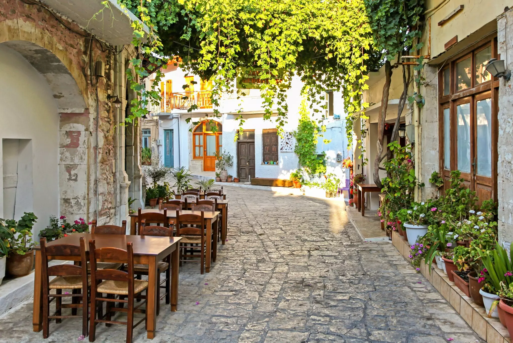 Tables and chairs outside a restaurant tucked down a narrow cobbled street covered in greenery.