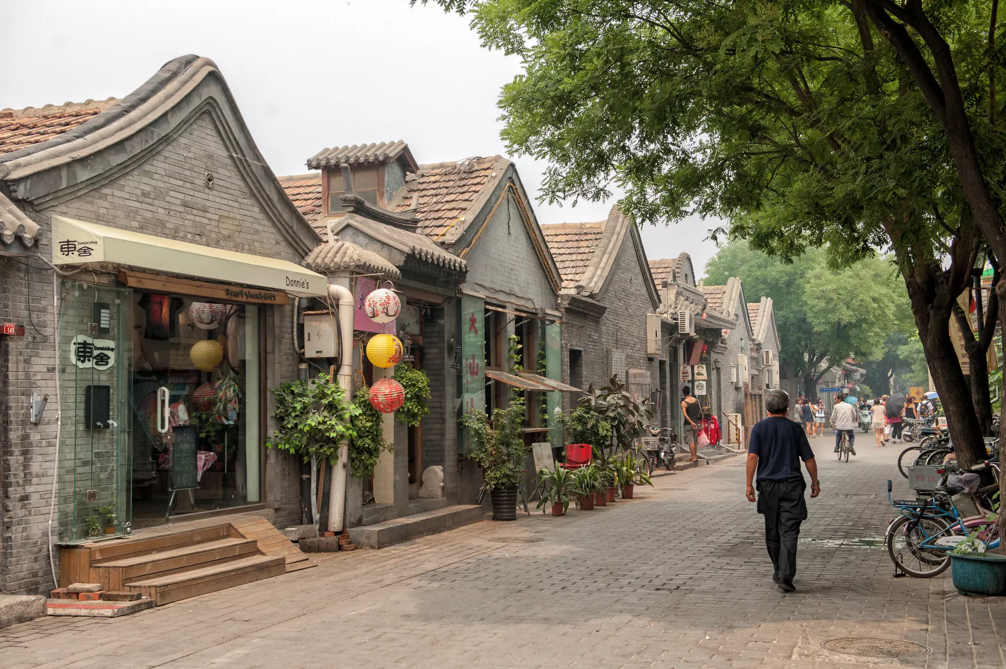 People and cyclists on a narrow street lined with small shops.