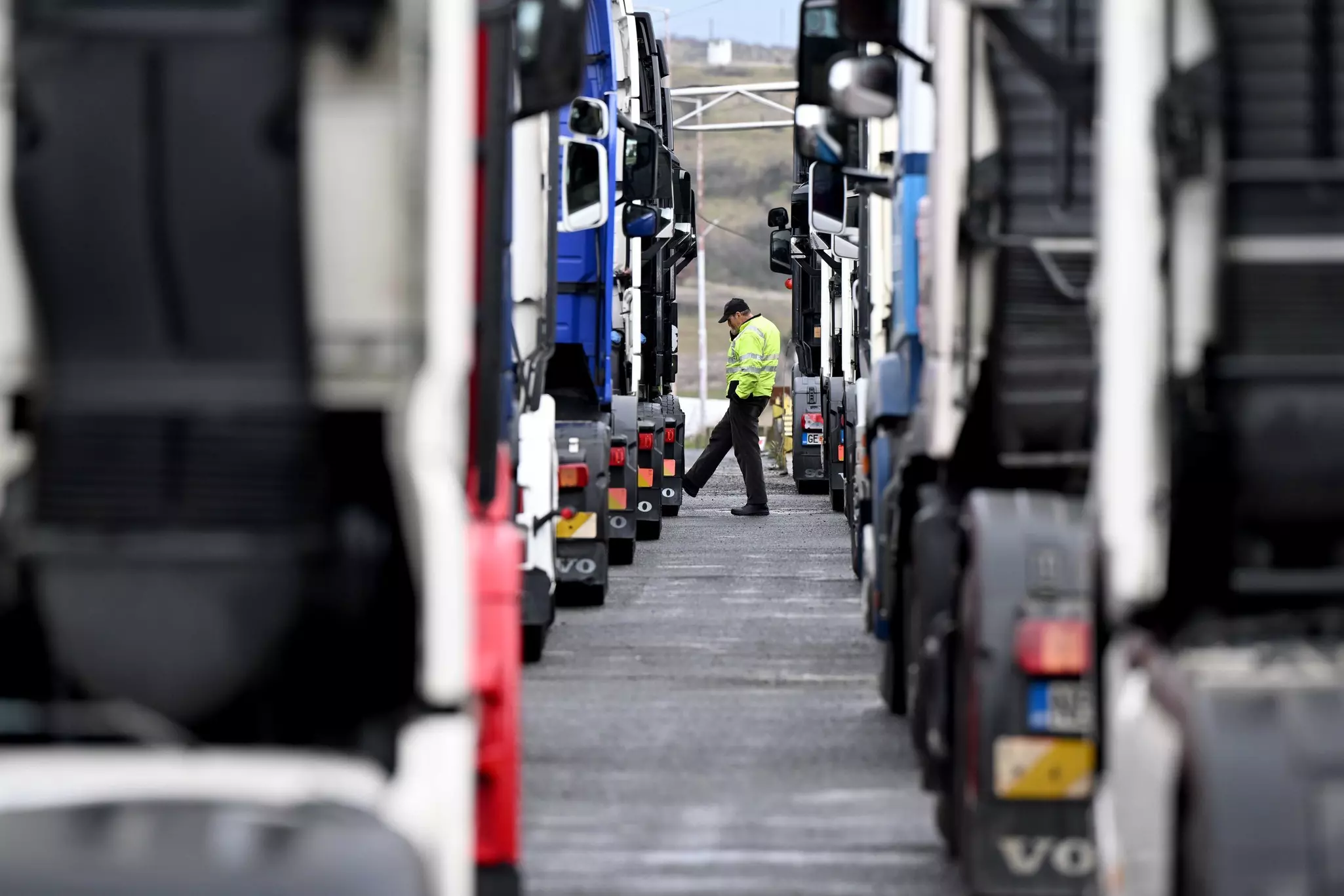 A man is seen in the distance between two queues of trucks parked on a road.