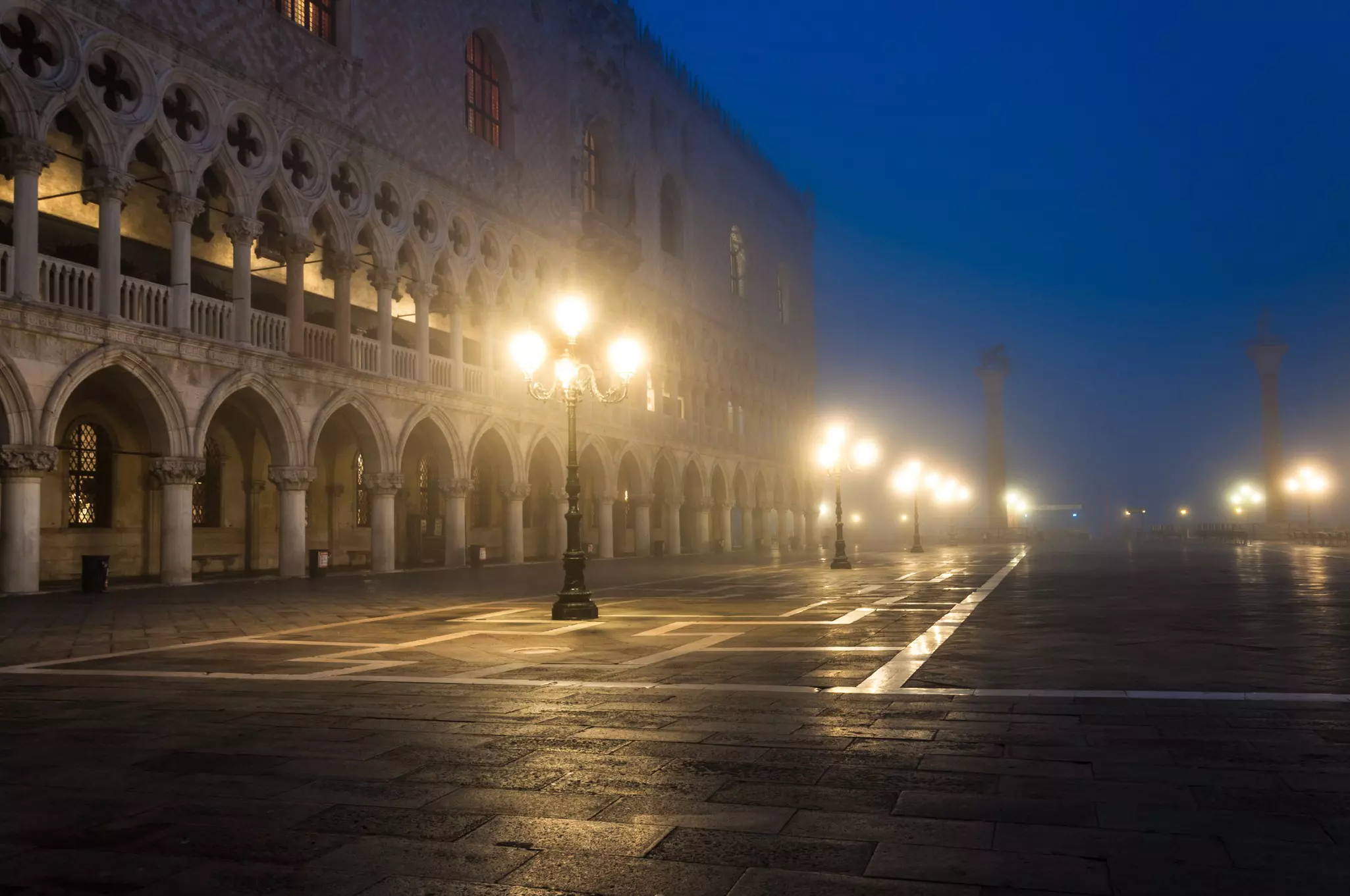 Lanterns illuminate a foggy evening in a square in a city.