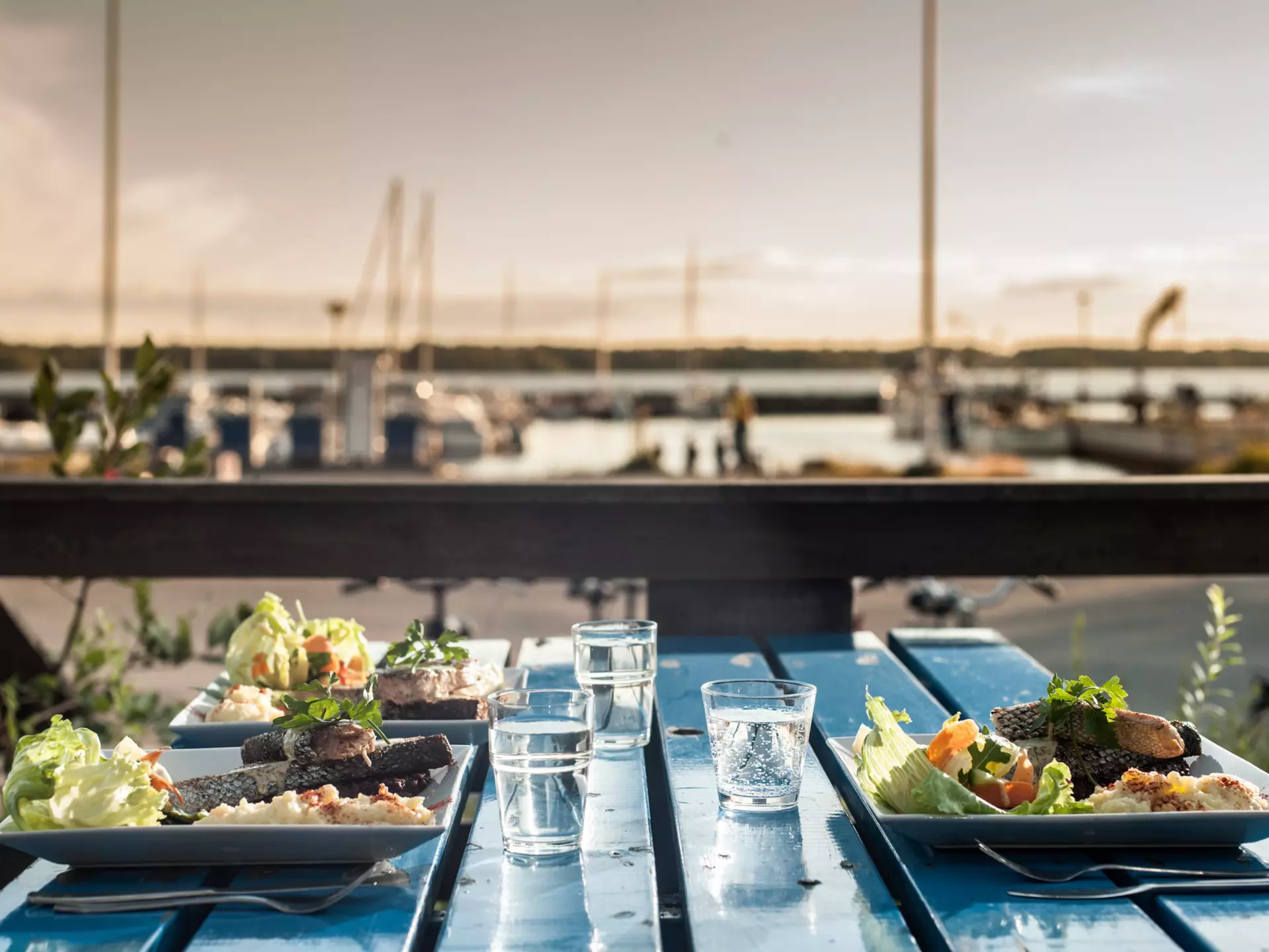 A table beside a marina laid for three people with three plates of fish and salad.