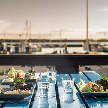 A table beside a marina laid for three people with three plates of fish and salad.