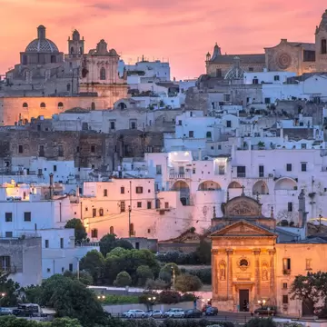 The whitewashed old town of Ostuni, topped by its domed cathedral, glows under a pink dusk sky in Puglia, Italy