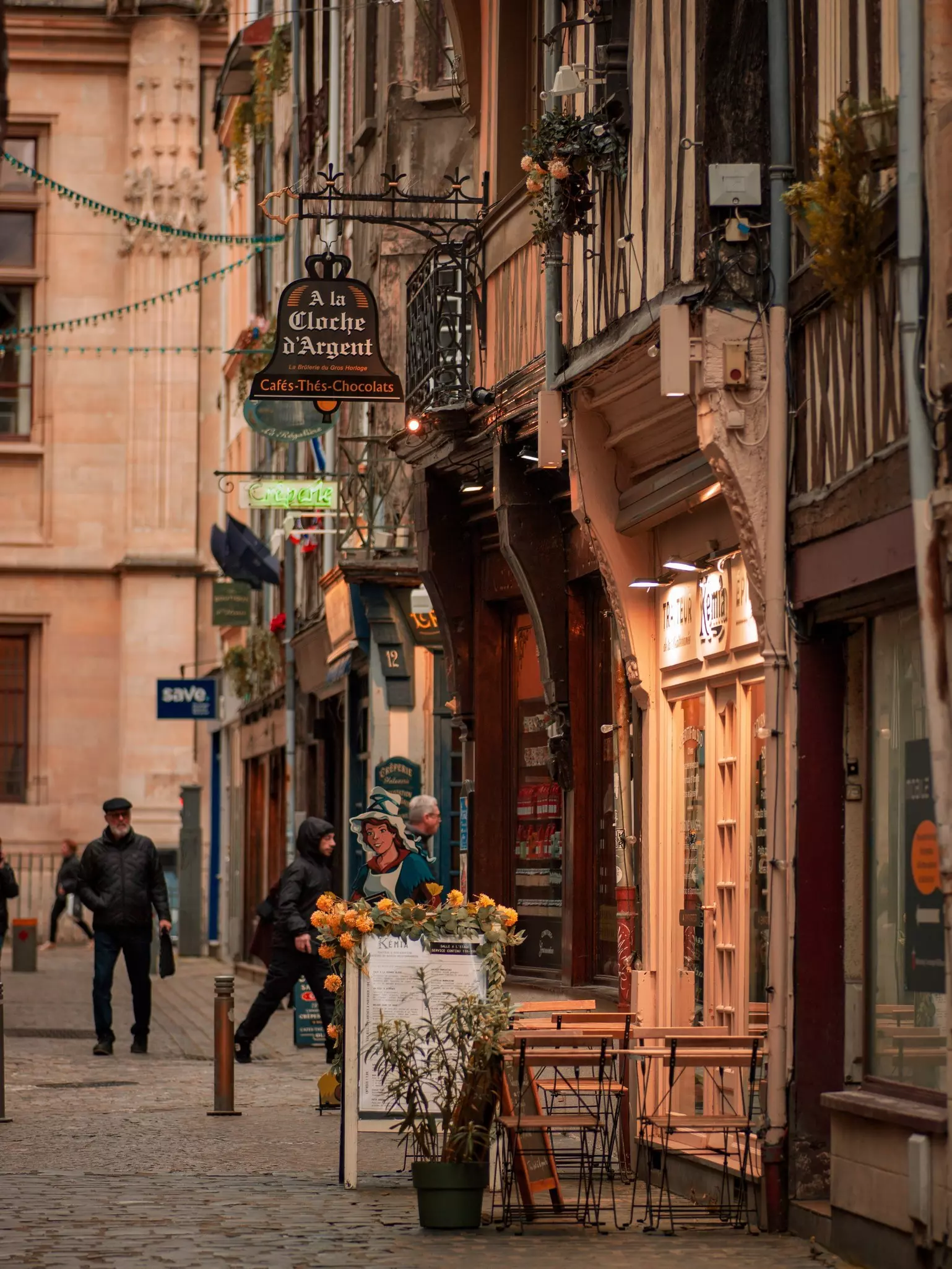 A historic, cobblestone street at dusk lined with cafes with small, outdoor terraces