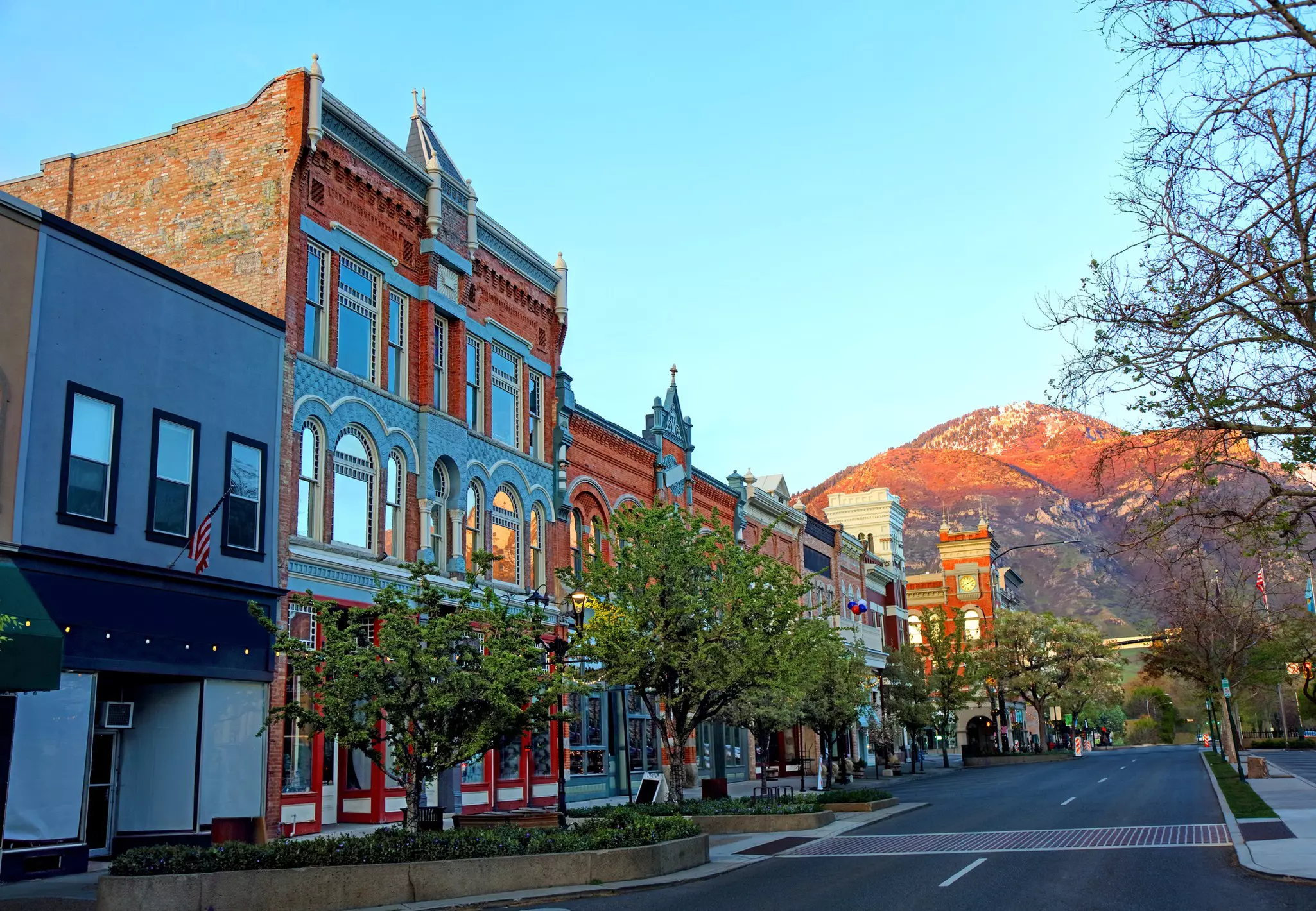 A strip of historic brick buildings lines a street in Provo, Utah in front of dramatic mountains
