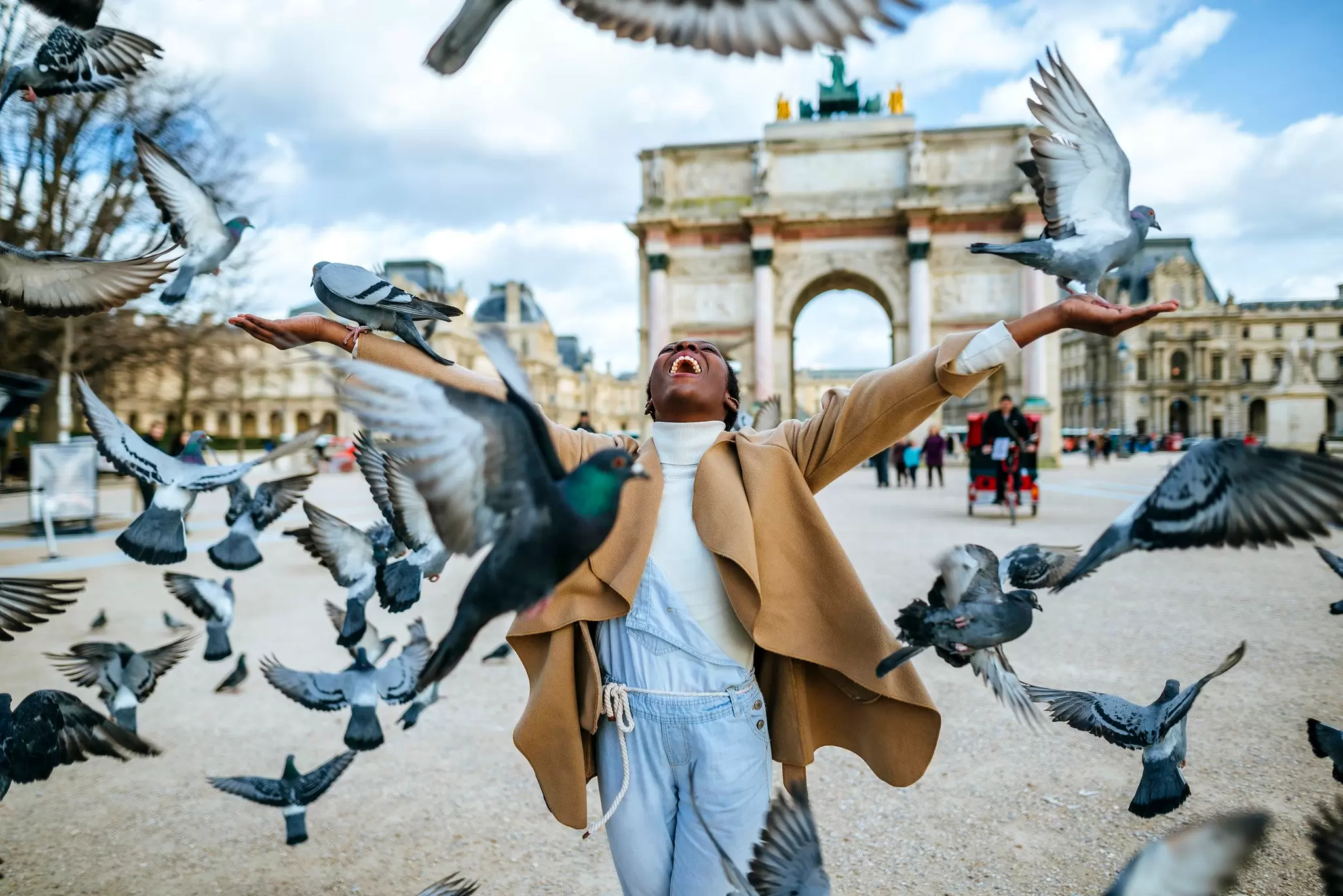 Joyful woman with outstretched arms feeding pigeons before the Arc de Triomphe du Carrousel in Paris