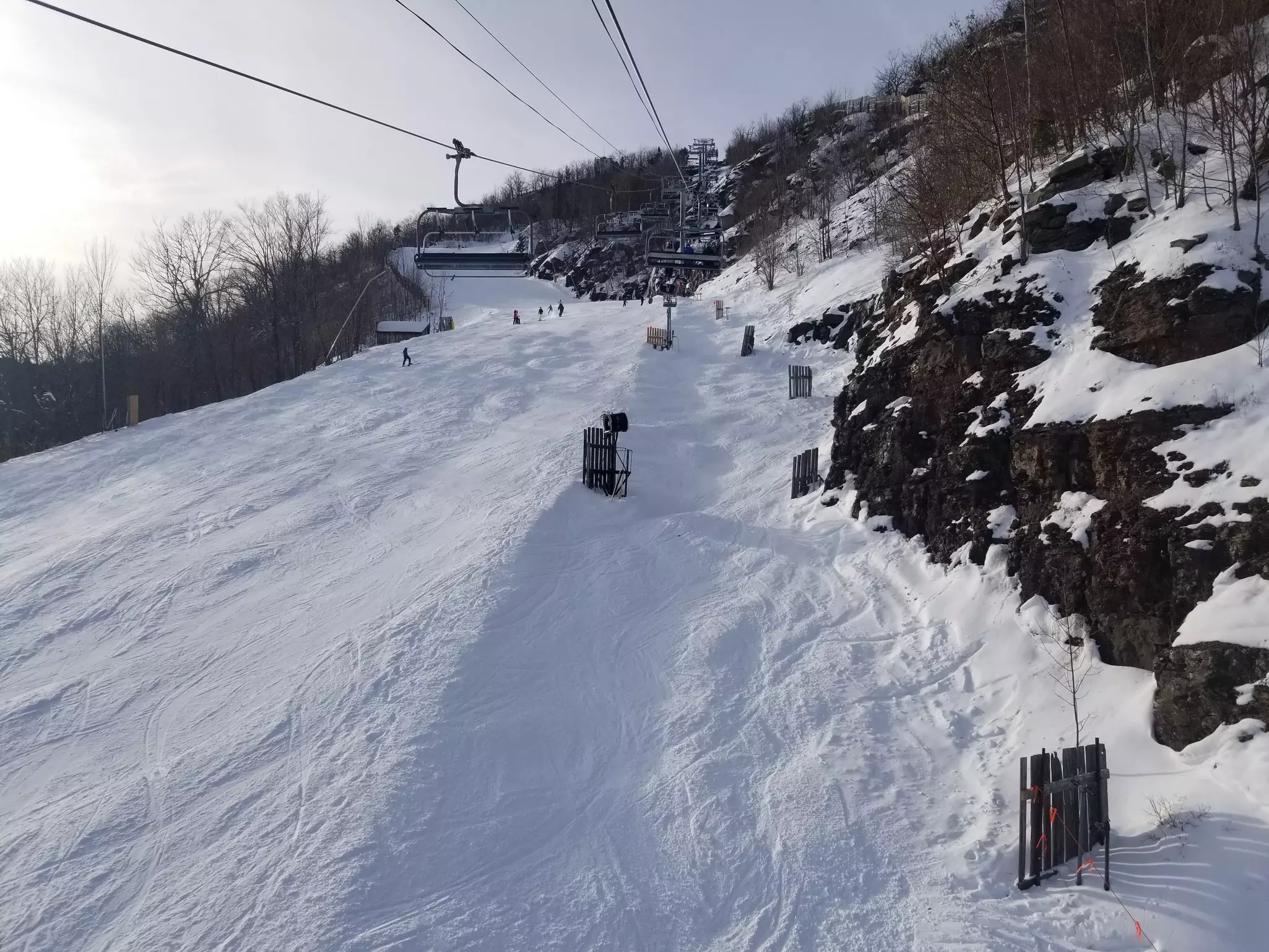A chair lift is pictured ascending a snow-covered ski slope on a cloudy winter day.