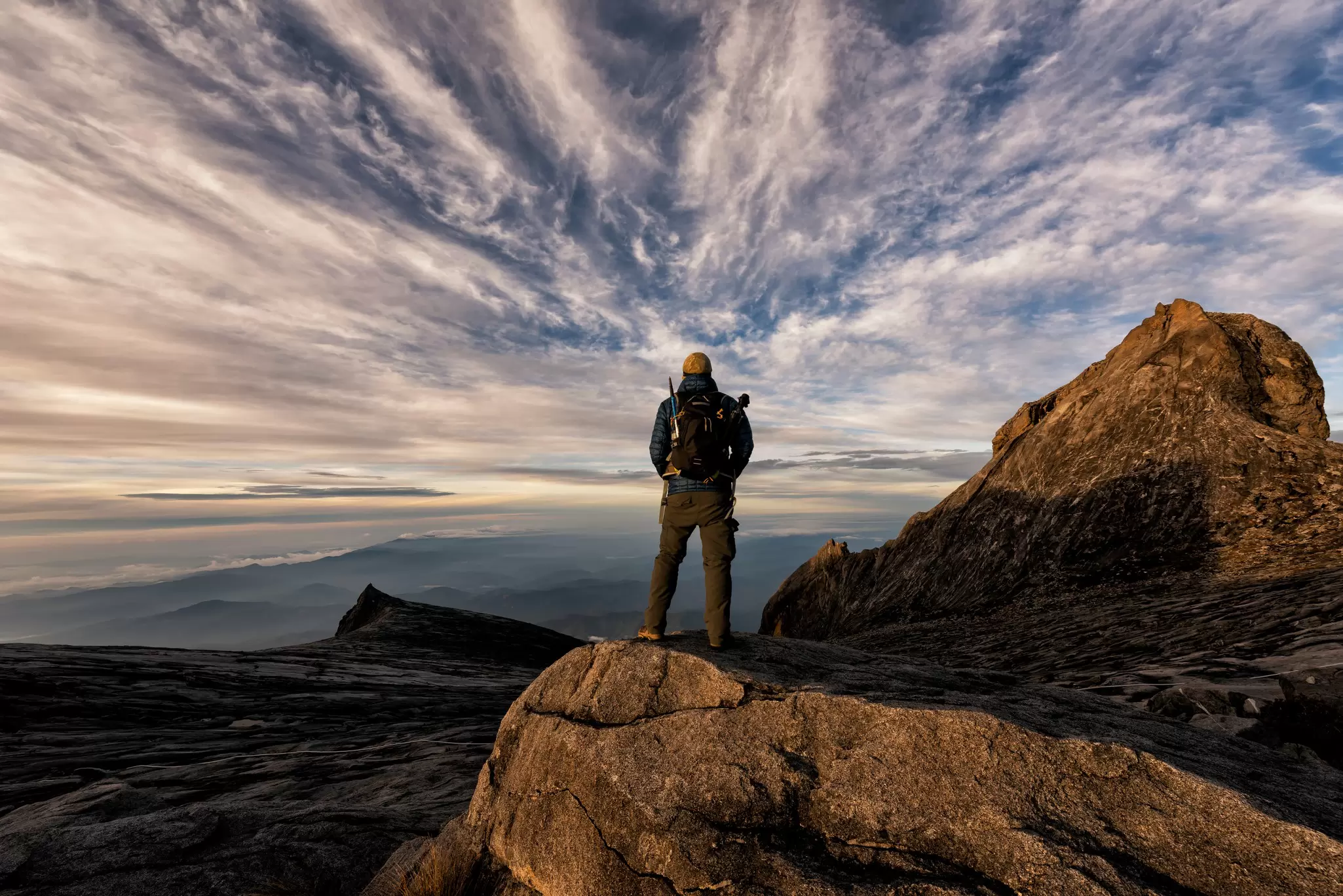 A hiker watching the sun rise at the top of a rocky peak.