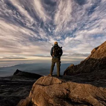 A hiker watching the sun rise at the top of a rocky peak.