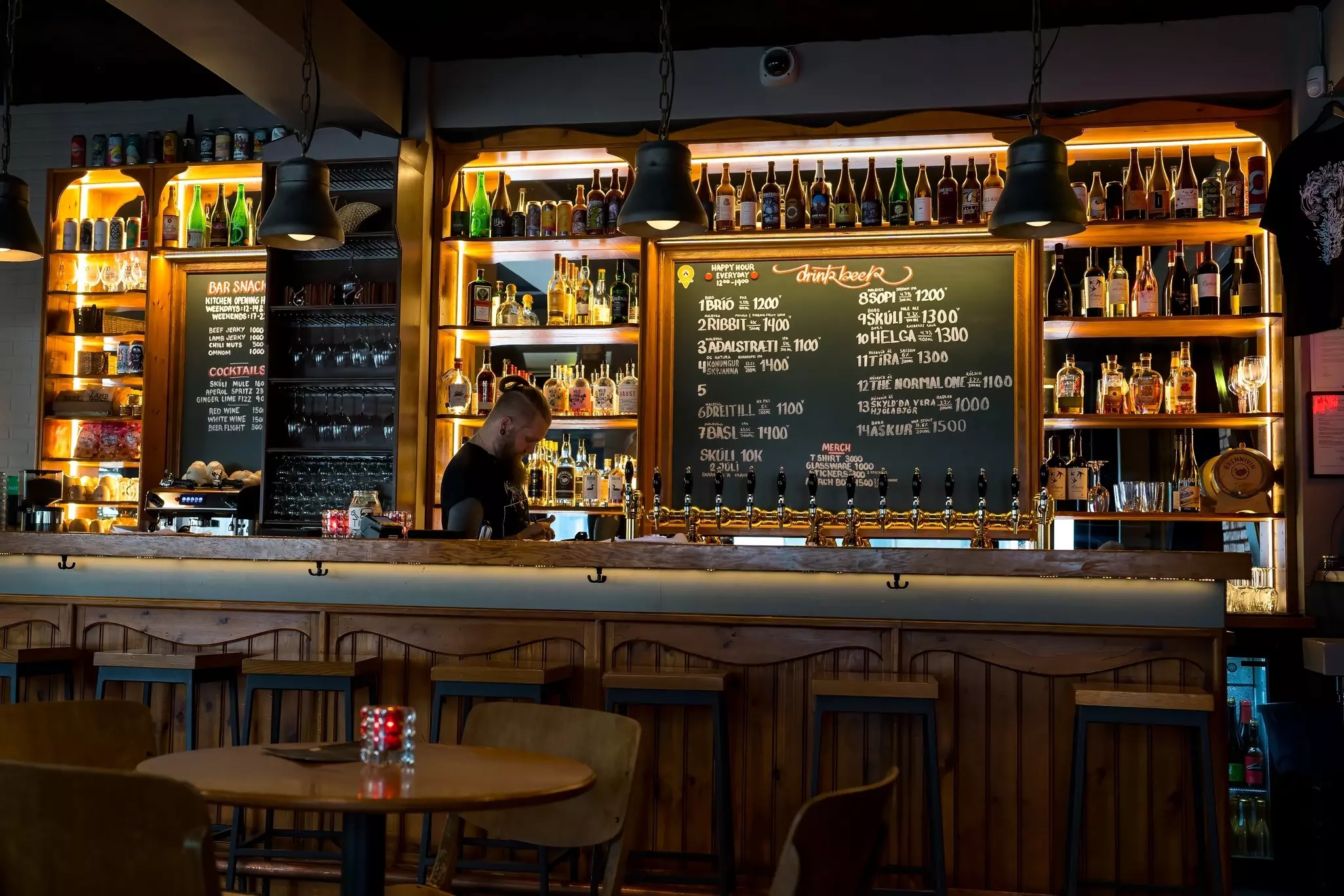 A man behind a bar, with bottles on the shelves and a blackboard menu.