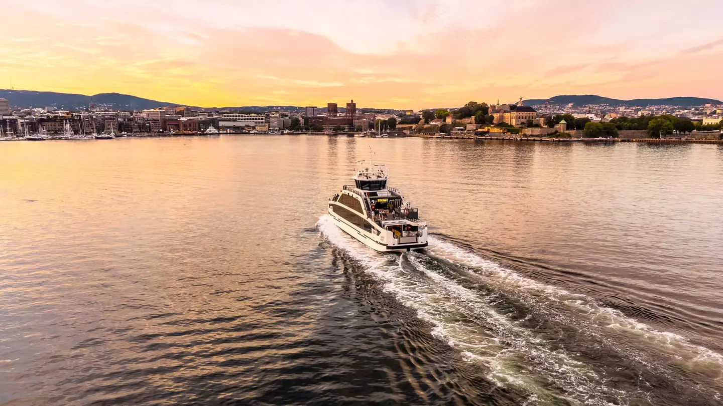 A small passenger boat traveling towards a city harbor as the sun sets.