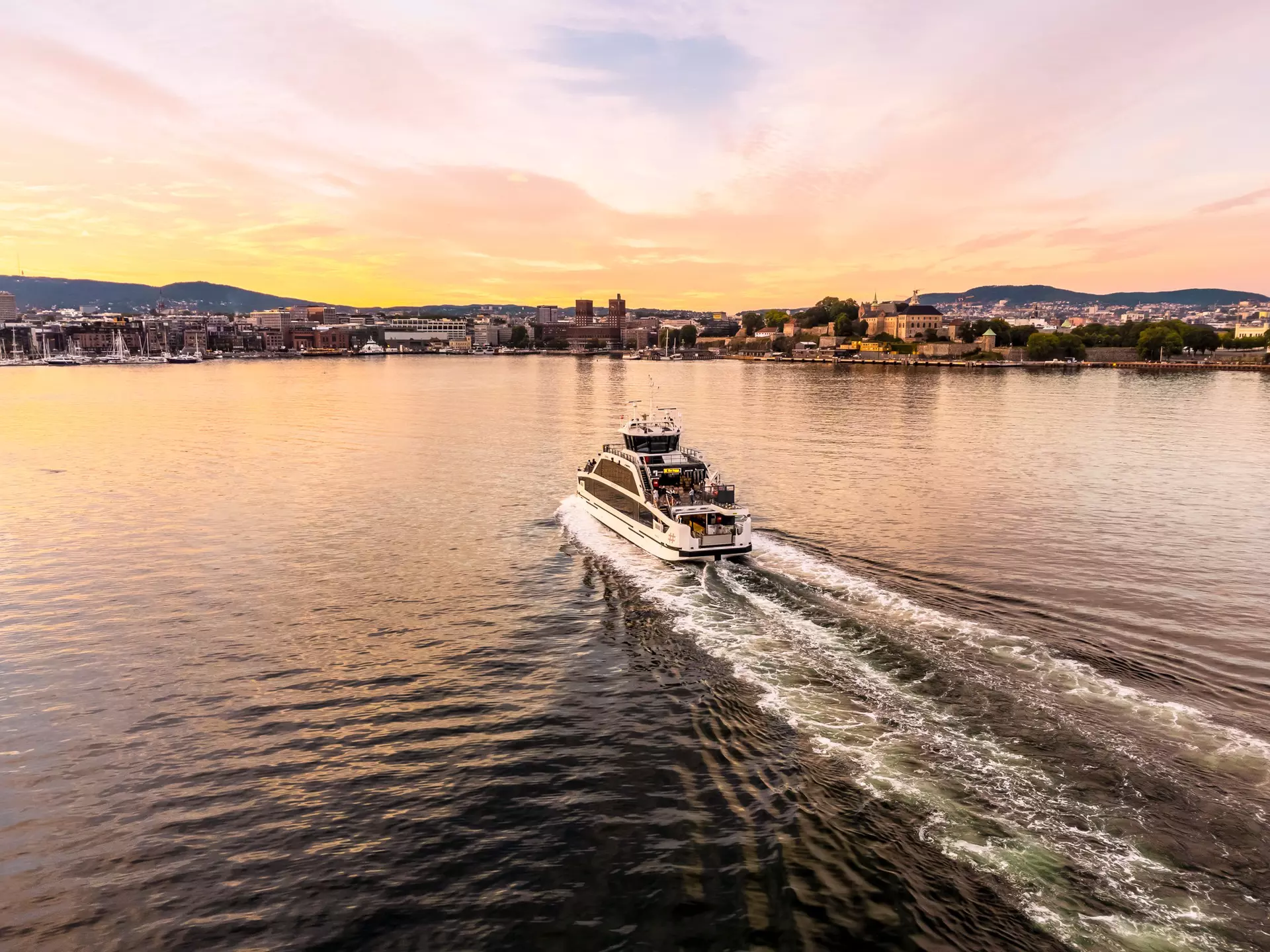 A small passenger boat traveling towards a city harbor as the sun sets.