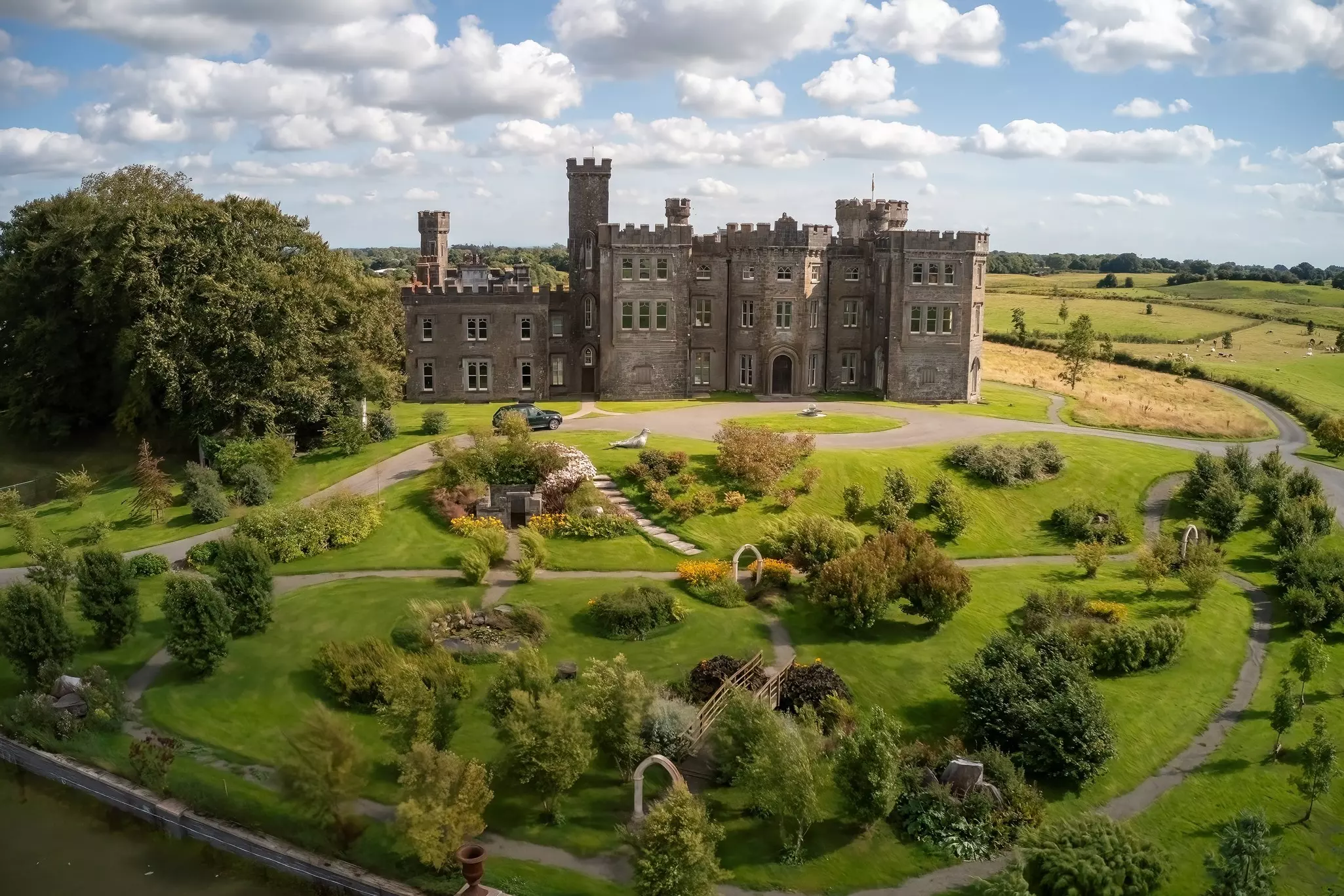 A large turreted castle standing in landscaped gardens of green lawns and bushes.
