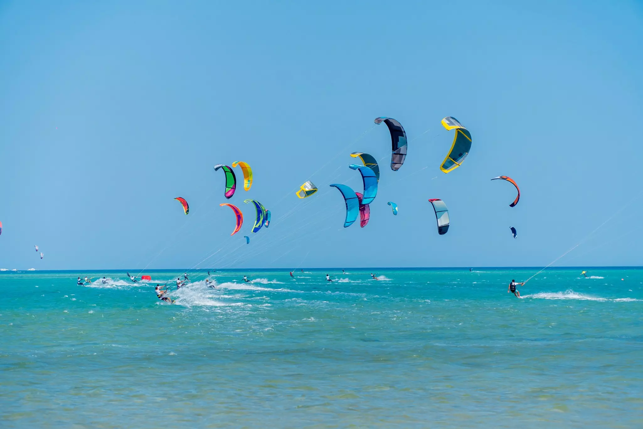 Many colorful kites in the sky attached to surfers on the ocean below.