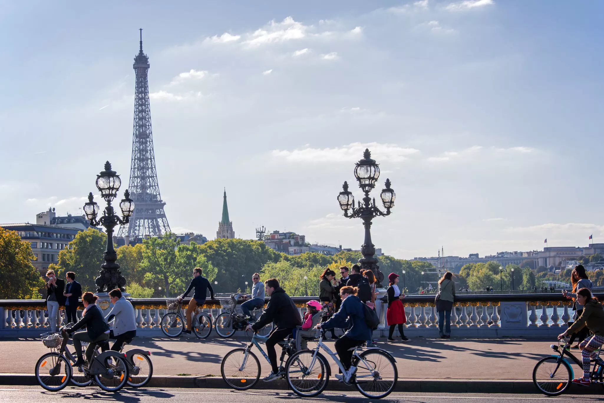 Cyclists pedal across a bridge on dedicated bike lanes. A tall iron tower stands above them.