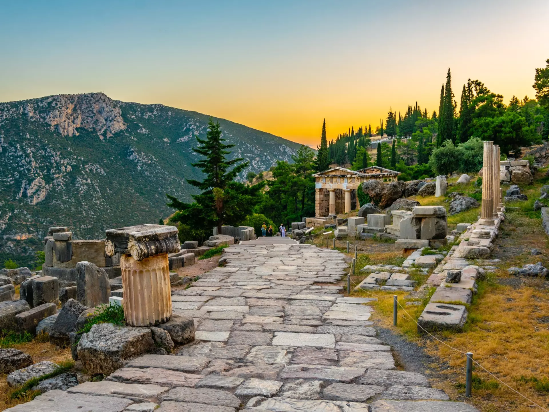 An ancient cobblestone pathway leads through ruins to a temple at sunset
