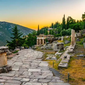 An ancient cobblestone pathway leads through ruins to a temple at sunset
