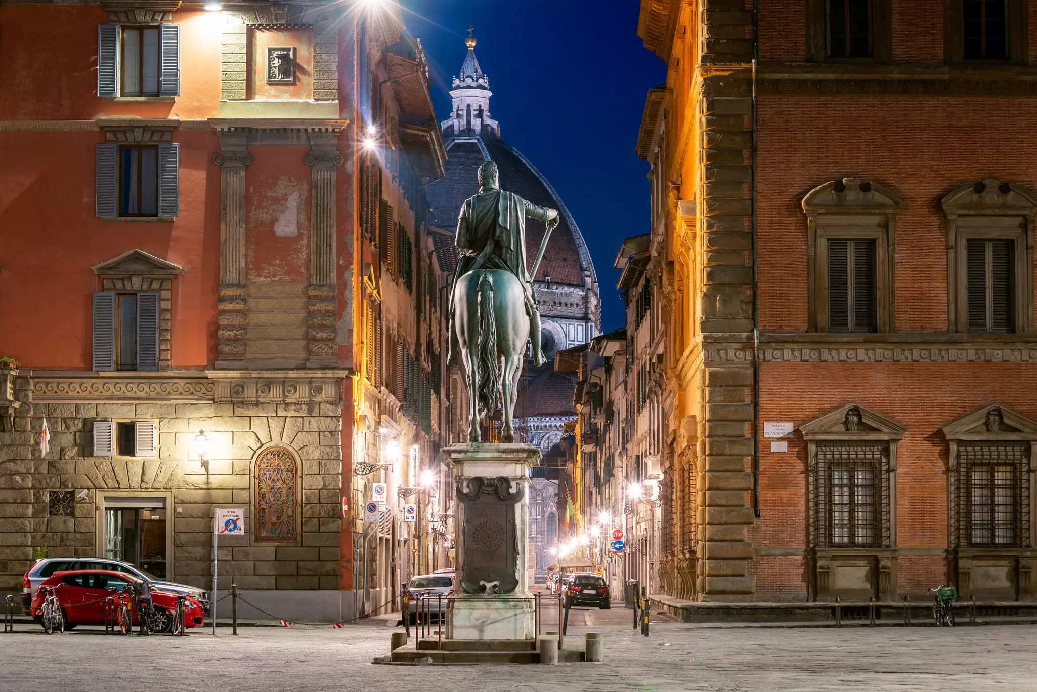 The back of a statue of a man on horseback in the evening light with a large domed building rising in the distance.