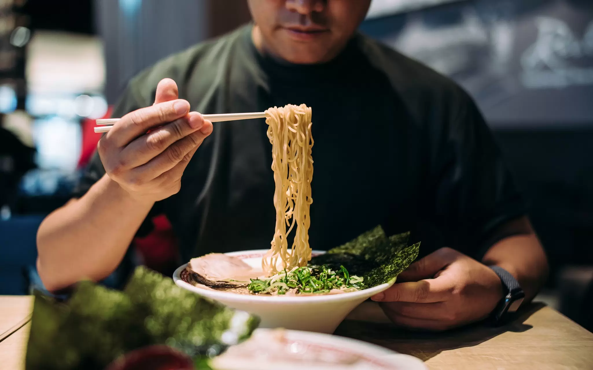 A man picks noodles out of a bowl with chopsticks.