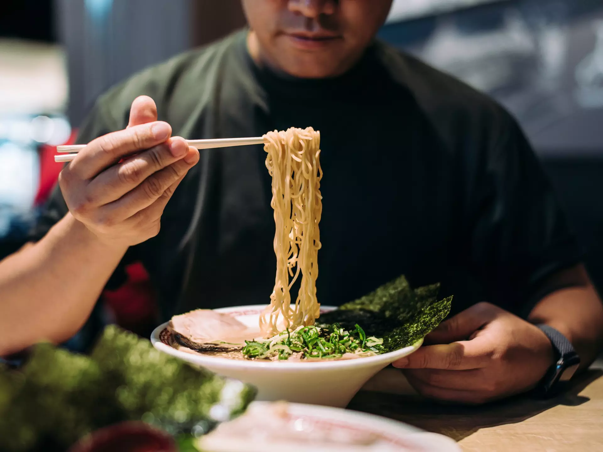A man picks noodles out of a bowl with chopsticks.