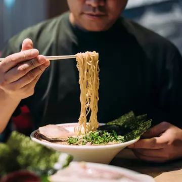 A man picks noodles out of a bowl with chopsticks.