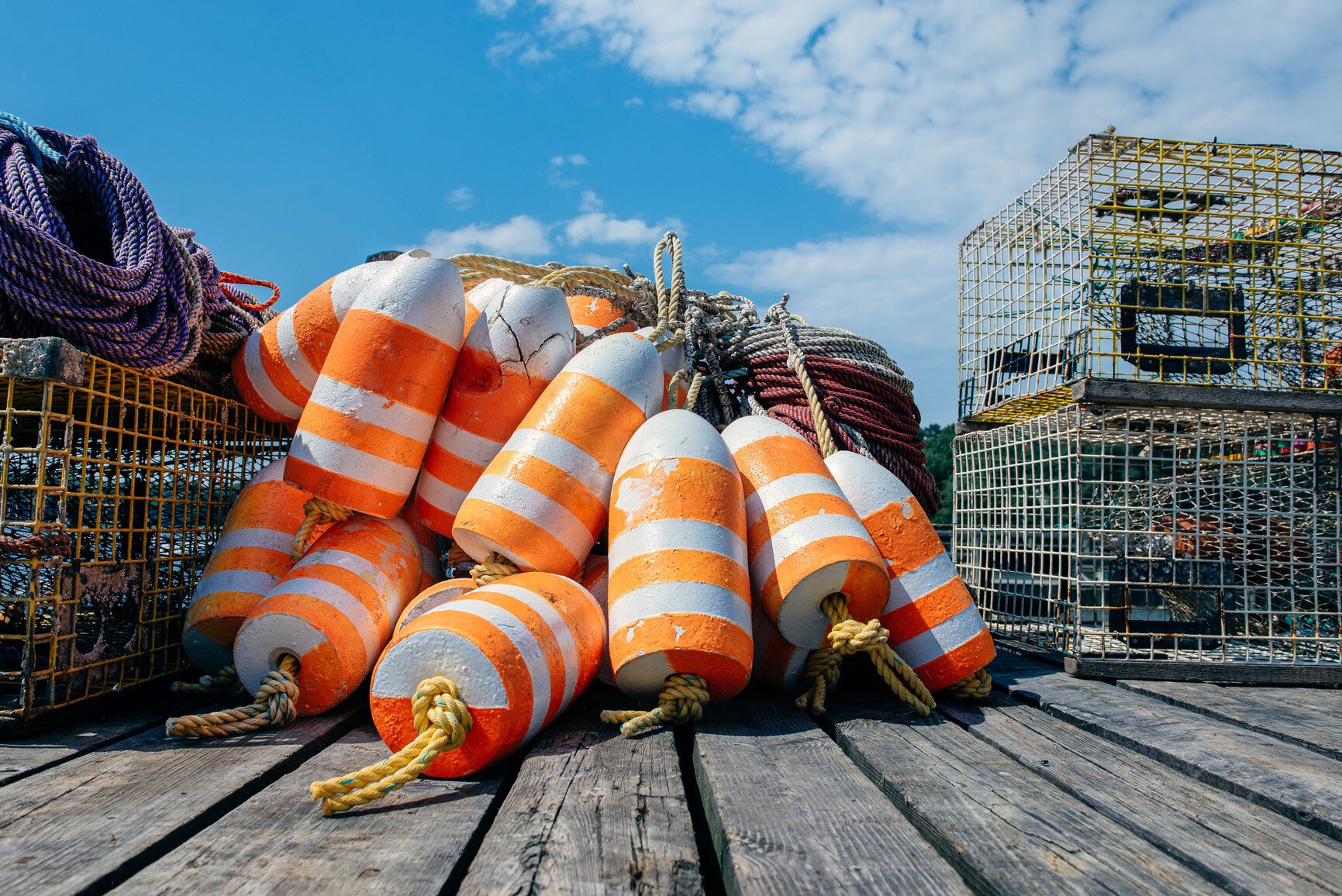 Pile of orange and white lobster trap buoys and traps on a dock