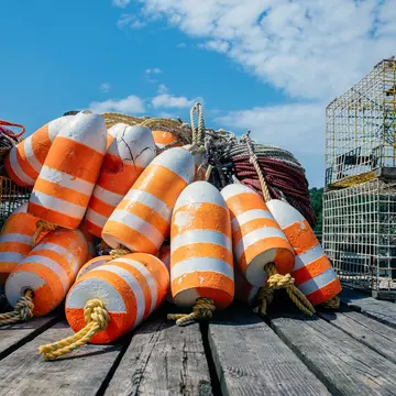 Pile of orange and white lobster trap buoys and traps on a dock