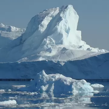 Massive white icebergs and floating ice fragments reflected in still blue water of Ilulissat Icefjord, Greenland