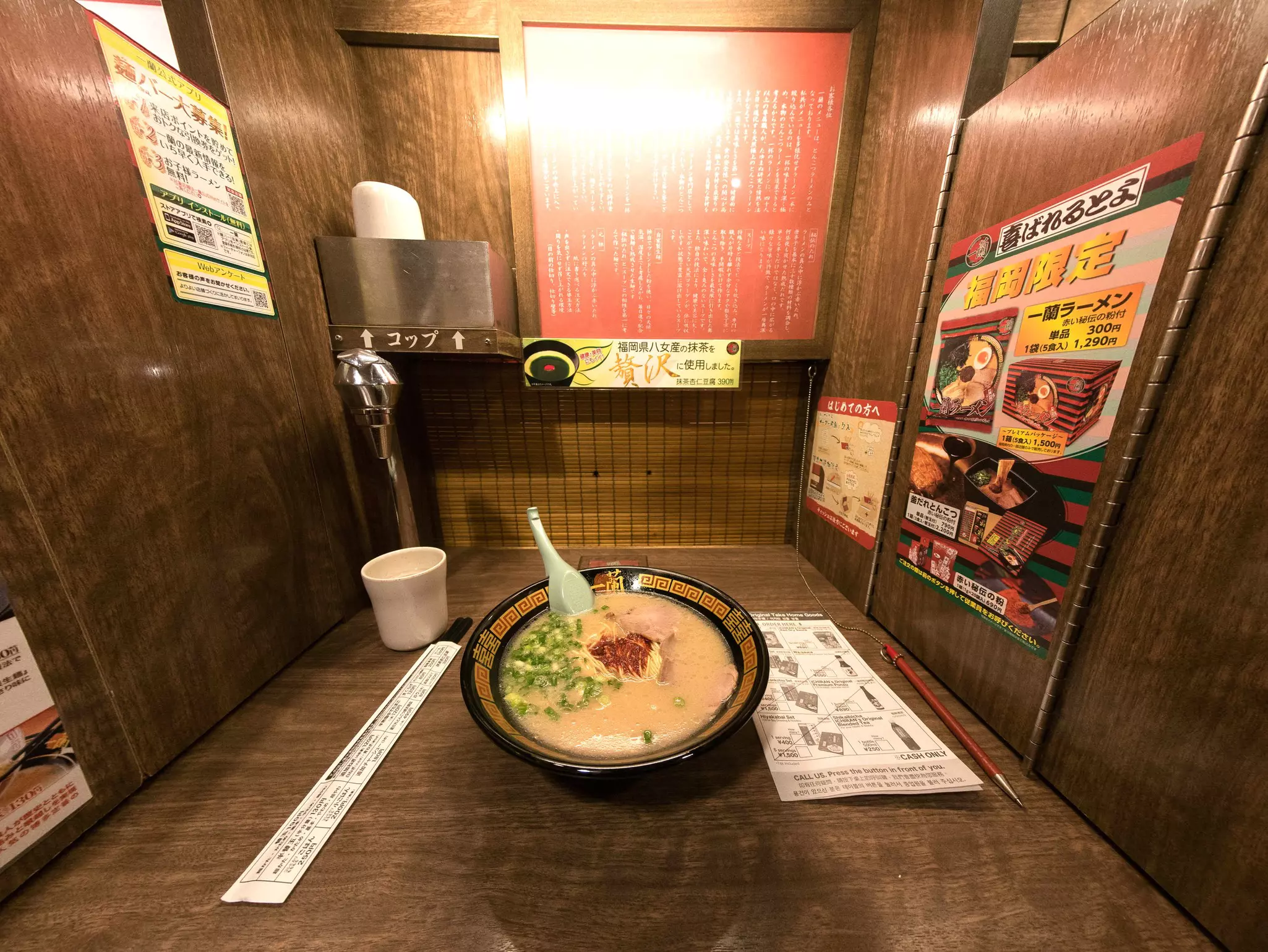 A bowl of ramen in a partitioned booth. Chopsticks lie on the left side of the bowl, and a menu lies on the right.