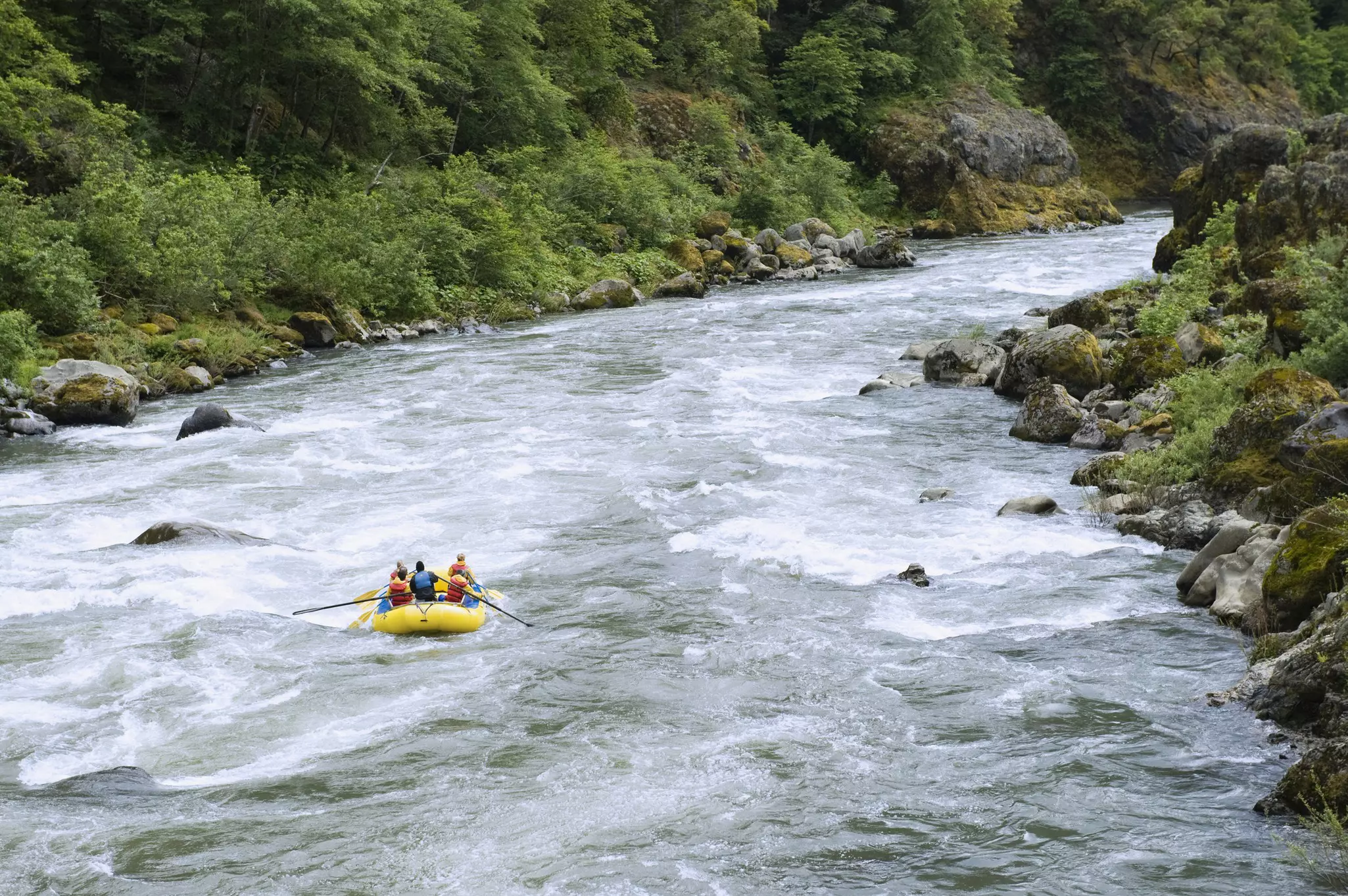A white water raft with passengers enters a frothy part of a river