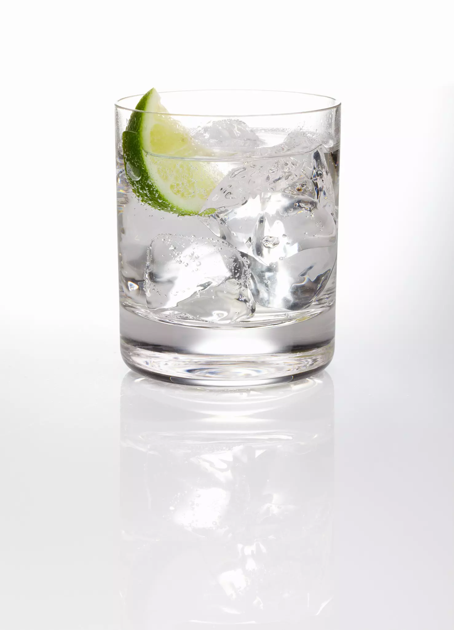 A glass of gin and tonic with ice and a slice of lime