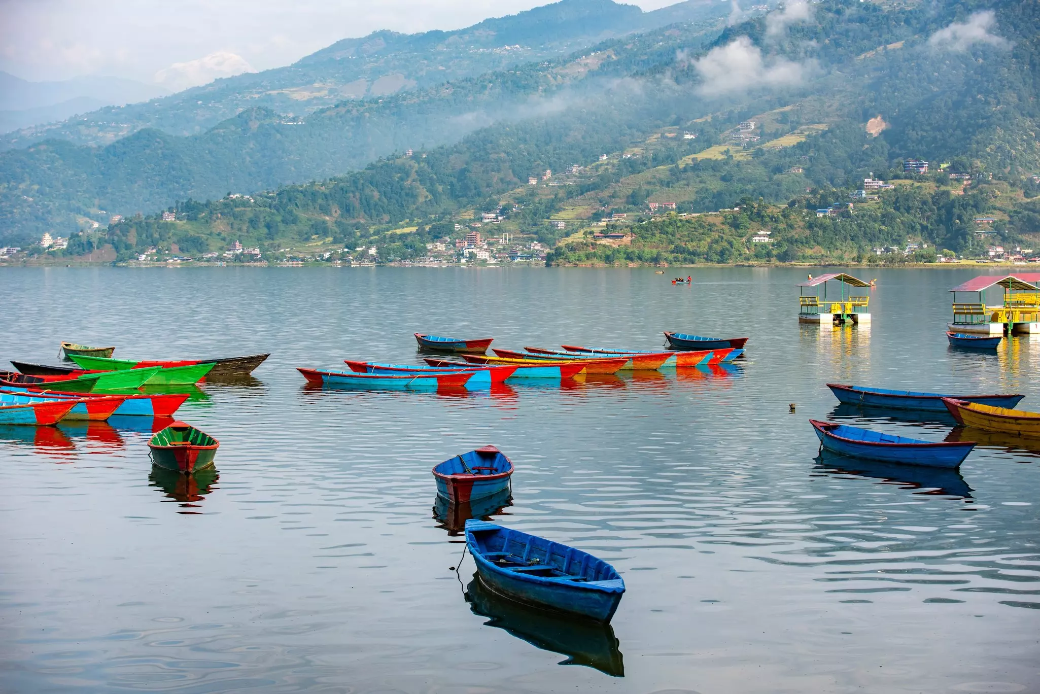 A lake with many colorful wooden row boats docked near the shore.