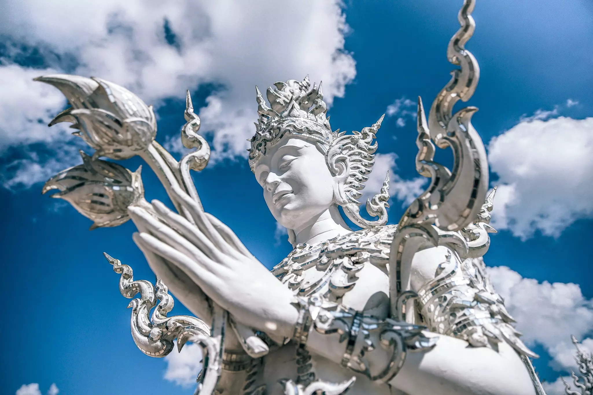 A white statue of a Buddhist deity at Wat Rong Khun in Chiang Rai, Thailand, with the cloudy sky in the background.