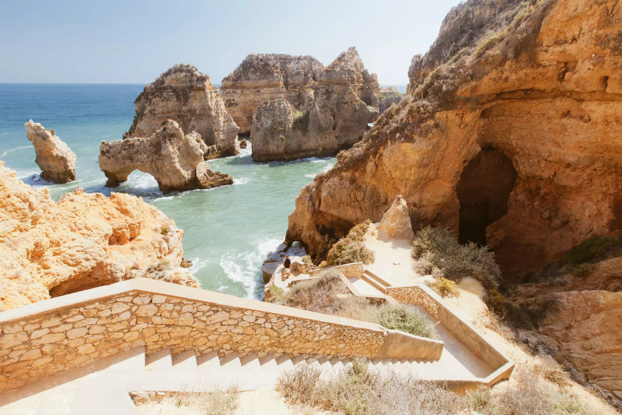Stone steps lead to the water by a headland in Lagos, Portugal, with dramatic cliffs and natural arch formations.