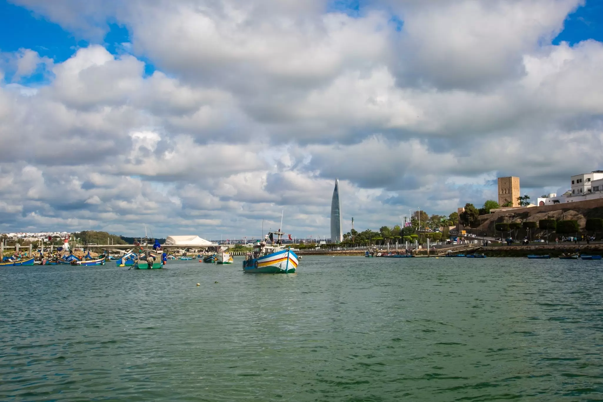 Boats in the water; a tall tower is on the right shore in the distance.