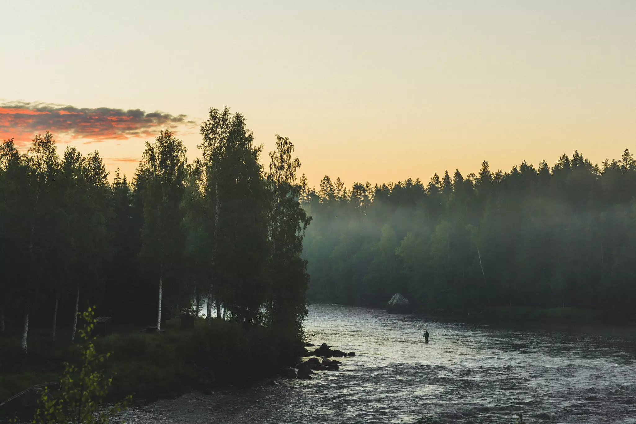 A solitary man fishes with a fly rod in a river in Sweden.