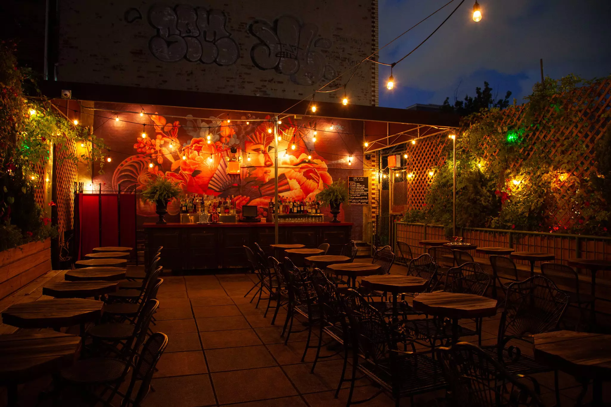 Tables on a roofdeck under strings of lights at night.