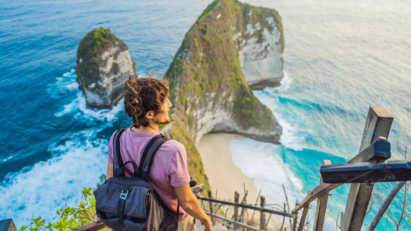 Man stand at viewpoint overlooking at beautiful Kelingking Beach on Nusa Penida Island Bali